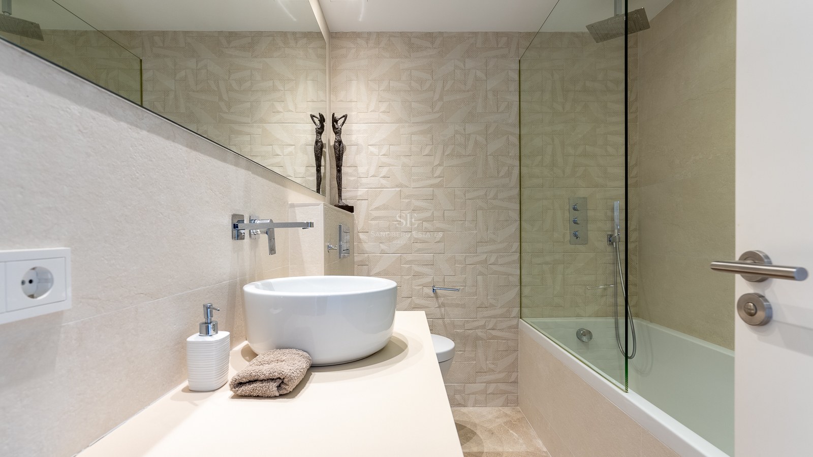 Salle de bains moderne avec vasque à poser, grand miroir et mur en carrelage géométrique texturé.