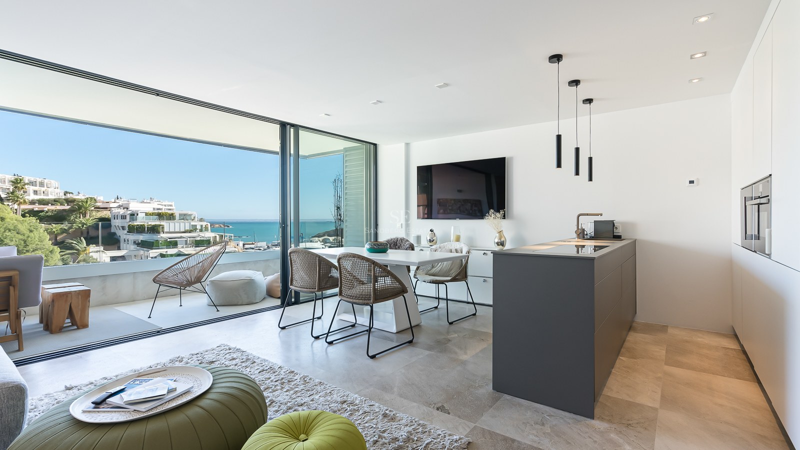 Espace de vie lumineux avec salle à manger, cuisine et baies vitrées ouvrant sur une terrasse face à la mer.