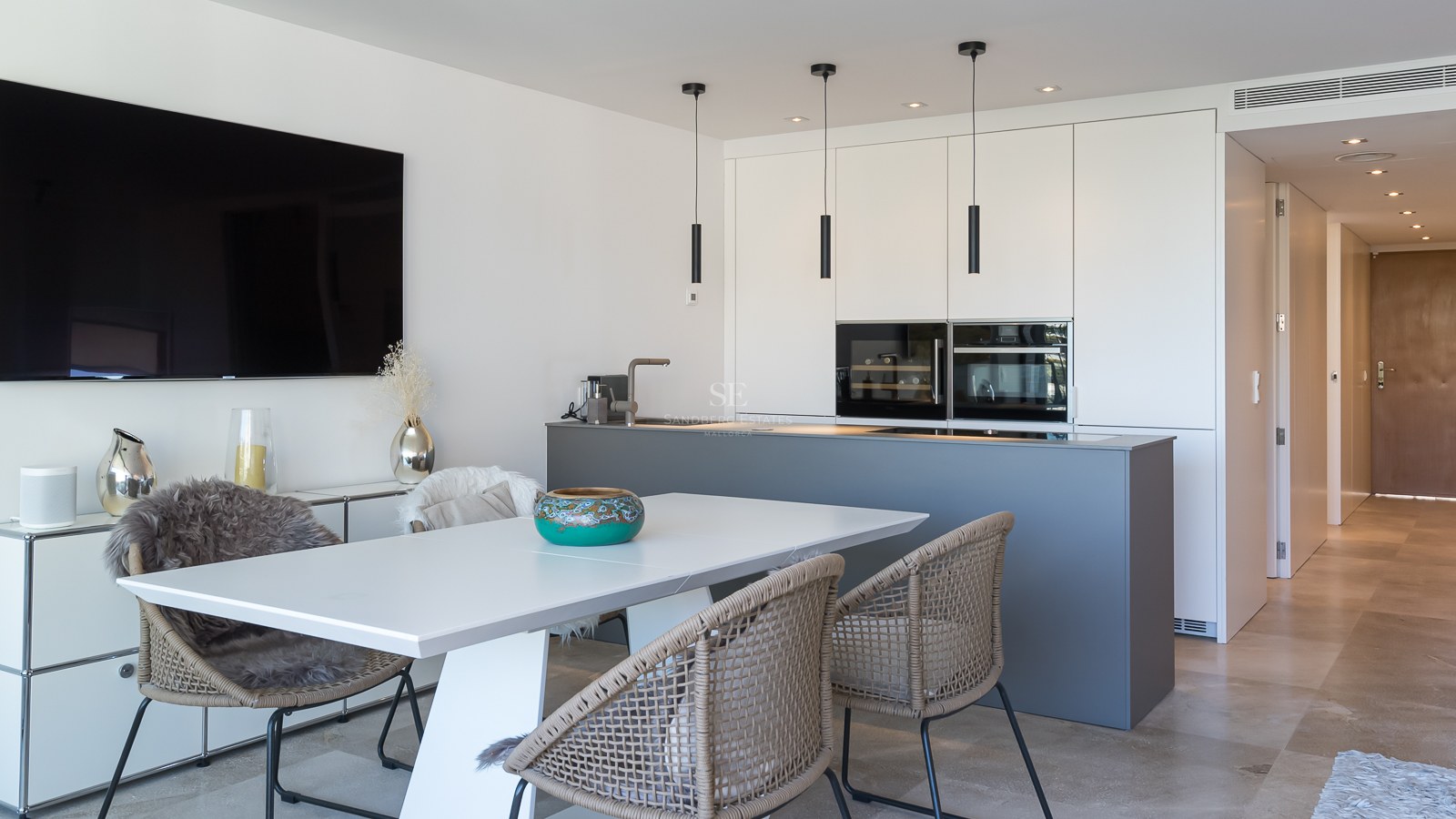 Cuisine moderne avec îlot gris, armoires blanches sans poignées et espace repas avec sol en pierre naturelle.
