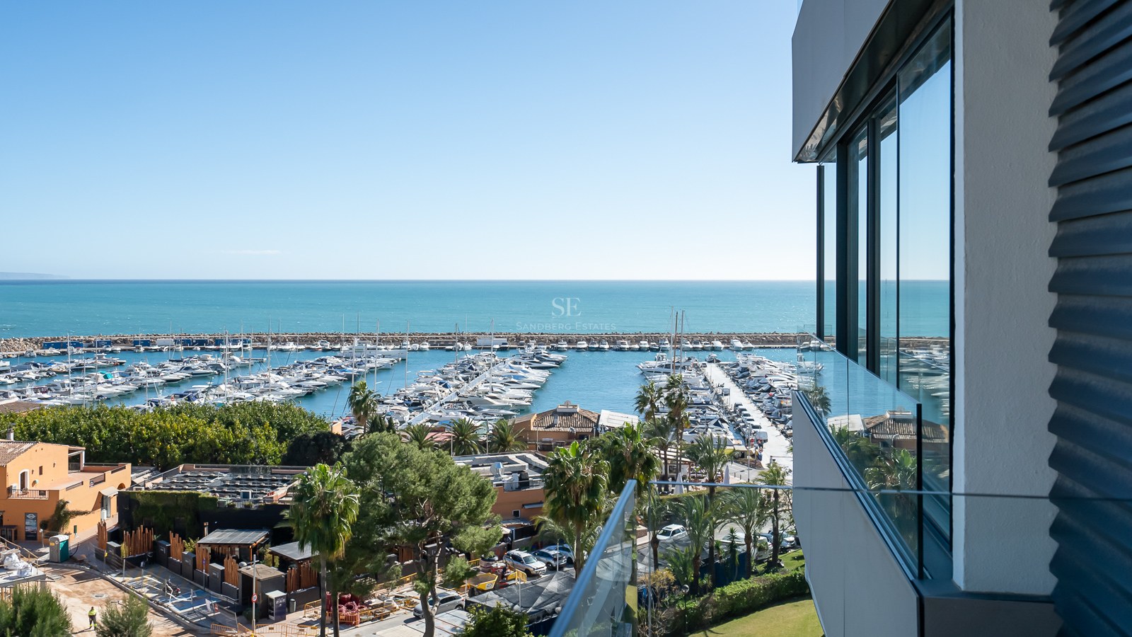 Vue surélevée depuis un balcon moderne donnant sur un port de plaisance et la mer Méditerranée.