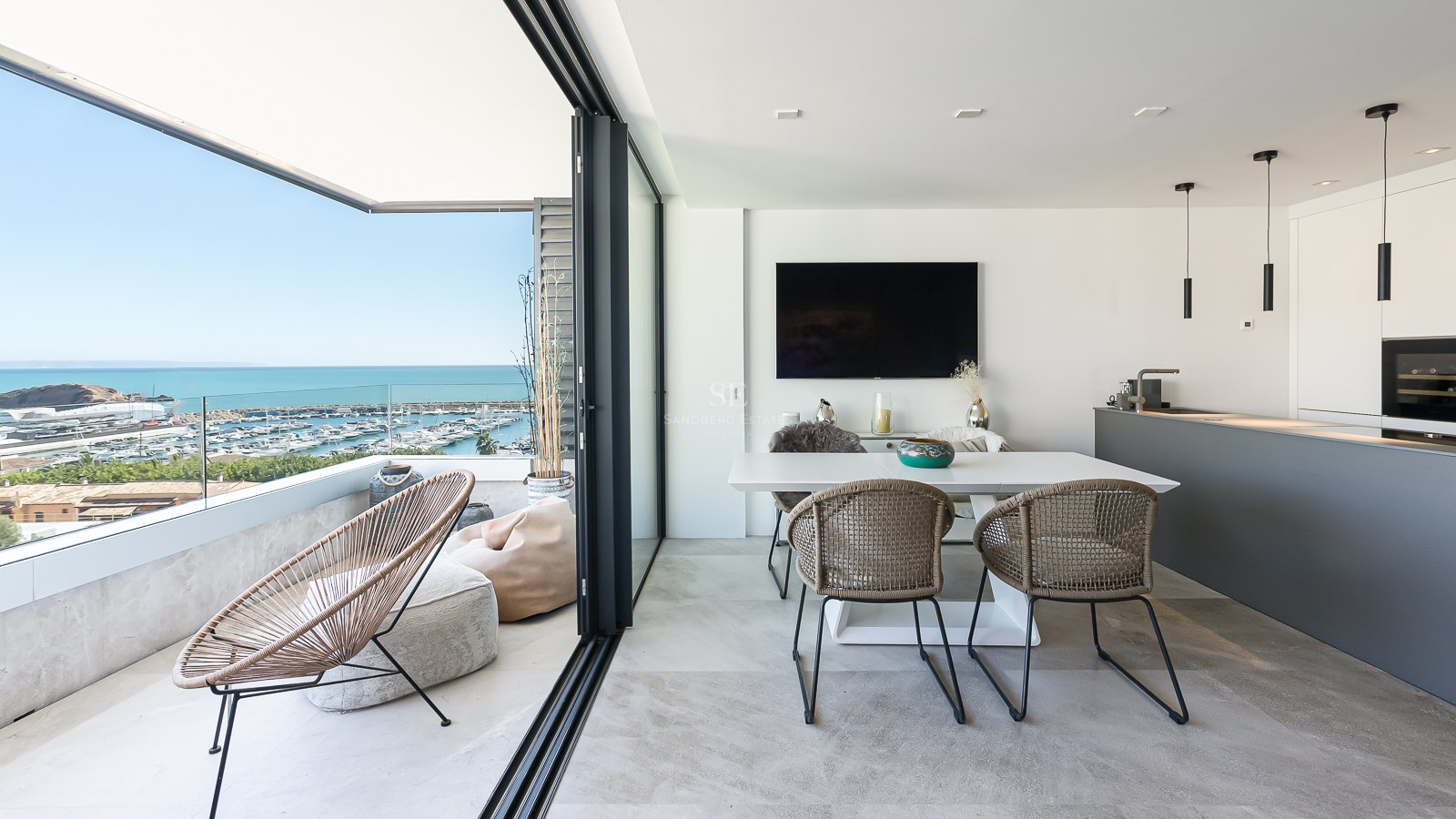 Salle à manger moderne et terrasse avec garde-corps en verre surplombant un port de plaisance et la mer Méditerranée.