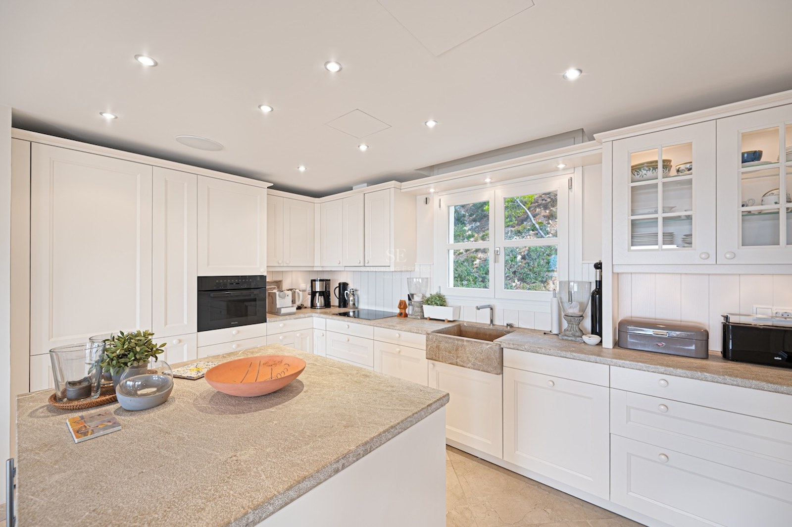Bright kitchen featuring white shaker cabinets, natural stone countertops, and integrated premium appliances.