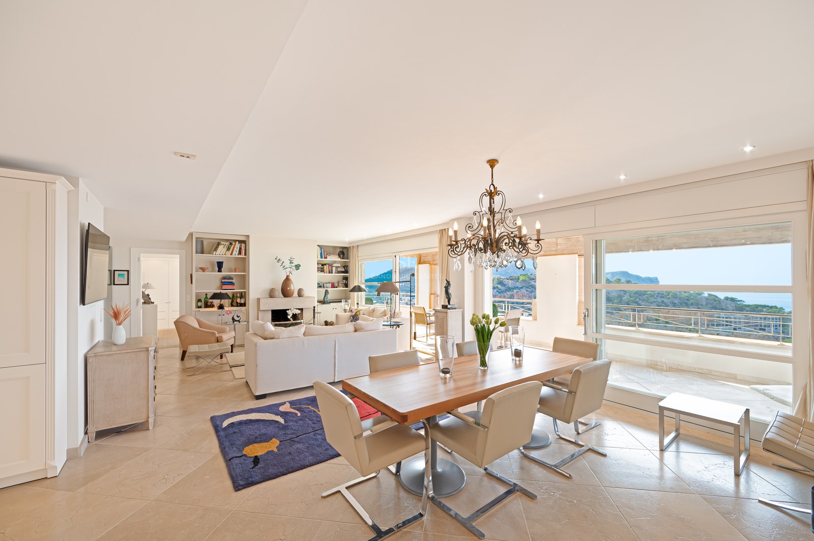 Bright open-plan living and dining room with marble floors, wooden table, and large windows overlooking the Mediterranean.