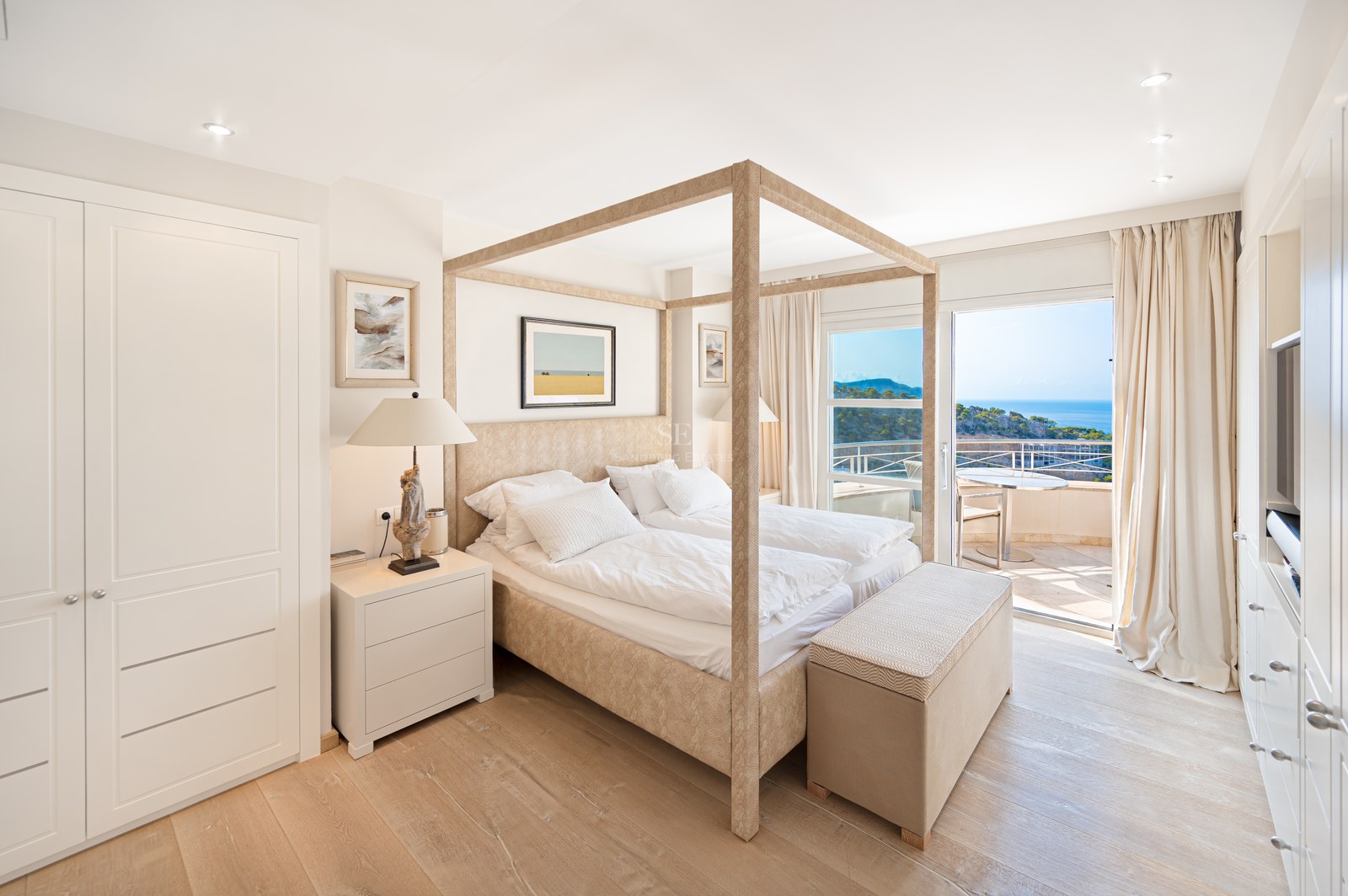Master bedroom featuring a light wood canopy bed, white bedding, and sliding glass doors opening to a sea-view terrace.