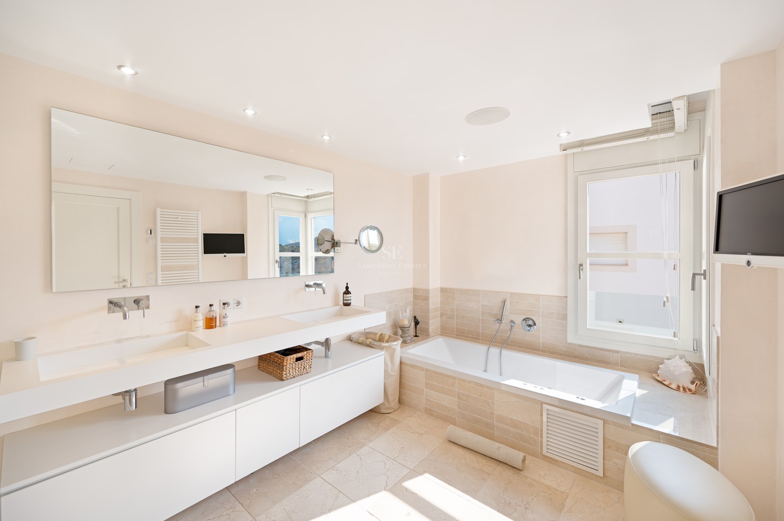 Bright master bathroom featuring a floating double vanity, large wall mirror, and built-in tub with neutral stone tiling.