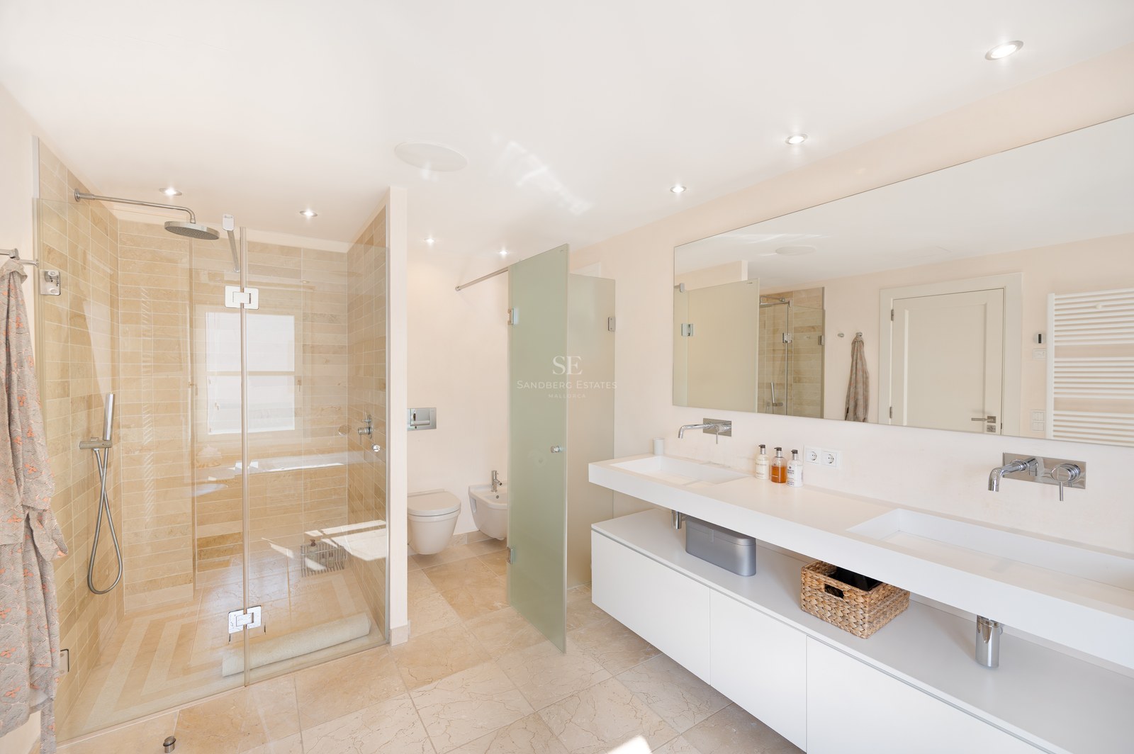 Bright bathroom featuring a double white vanity, large mirror, and walk-in shower with beige natural stone tiling.