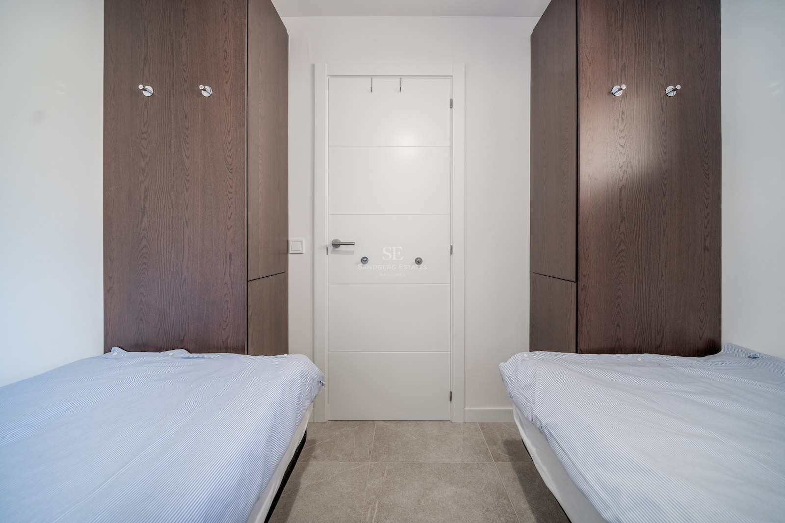 Chambre contemporaine avec lits jumeaux, placards en bois sombre et sol en carrelage gris.