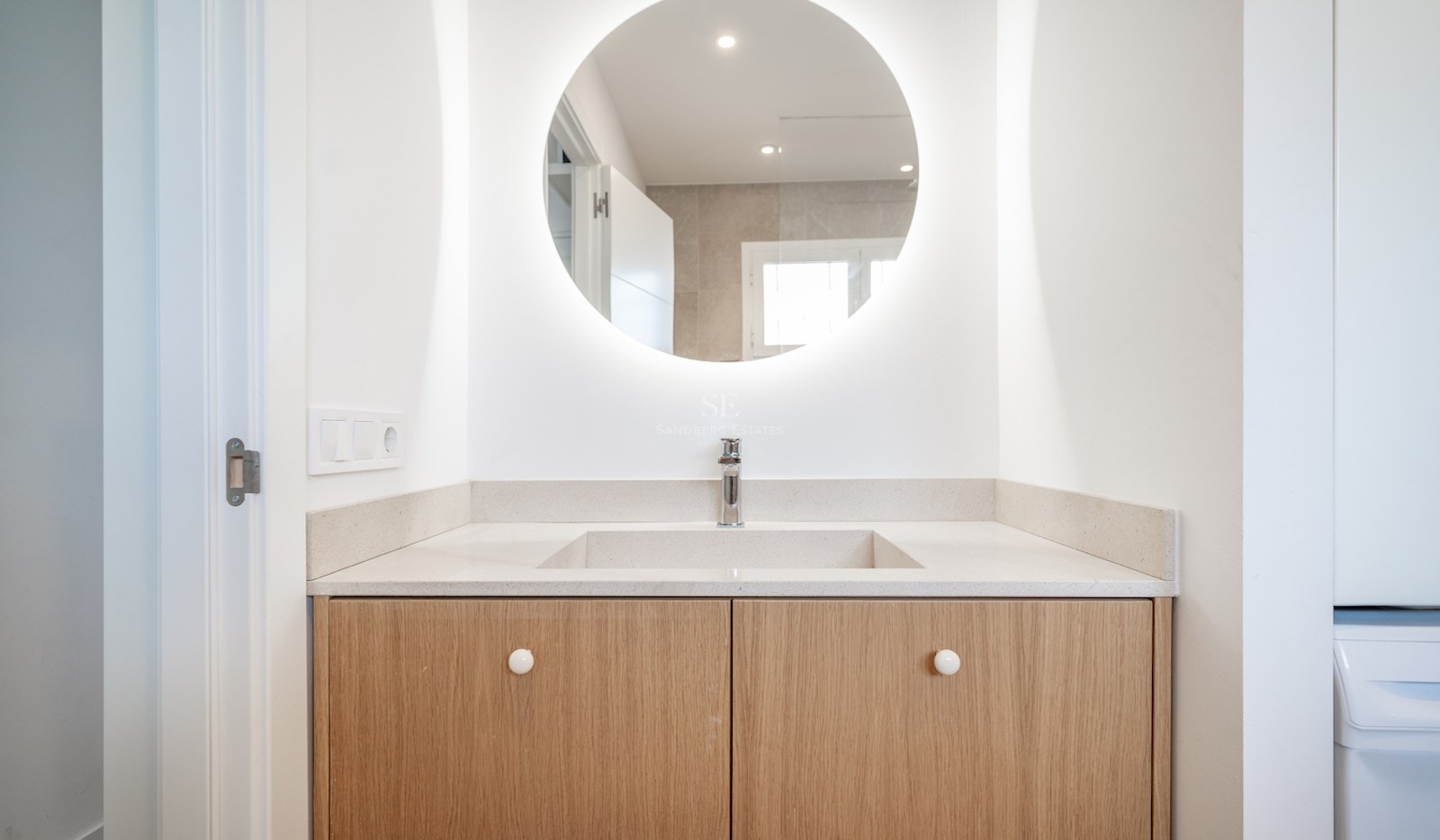 Vanité de salle de bain moderne avec miroir LED circulaire, ébénisterie en bois clair et lavabo blanc.