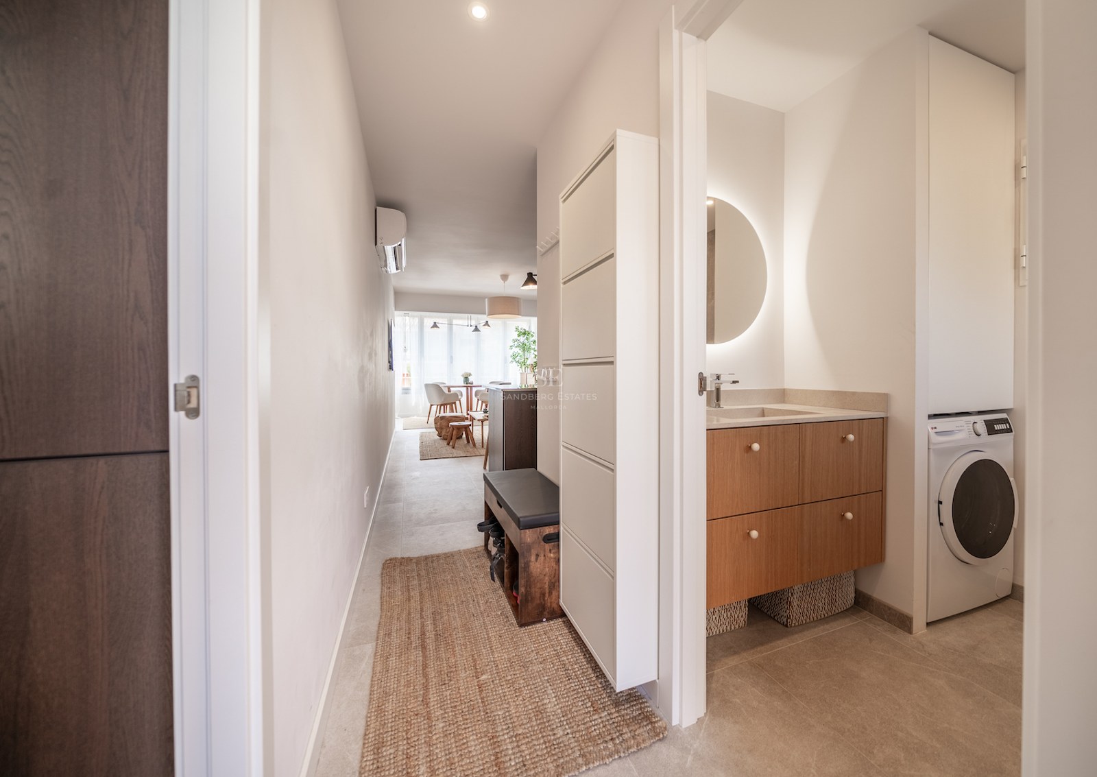 Couloir moderne avec meubles en bois clair, miroir rétroéclairé et tapis en fibres naturelles.