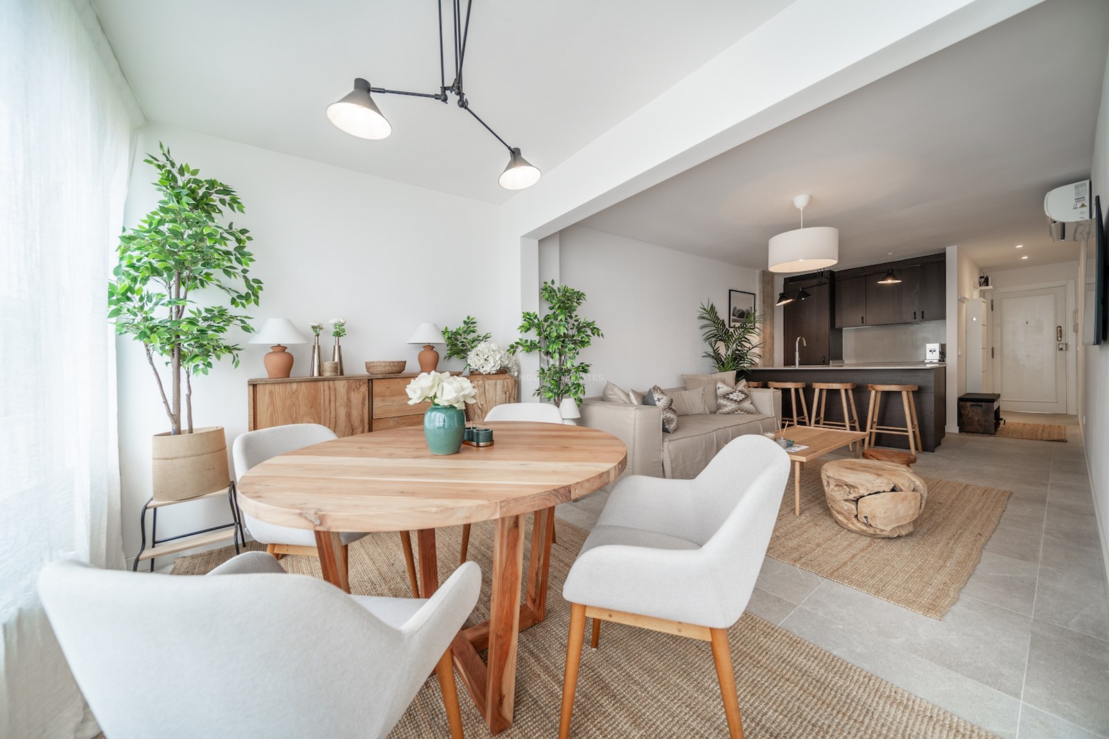 Salle à manger moderne avec table ronde en bois, chaises blanches et vue sur le salon et la cuisine ouverte.