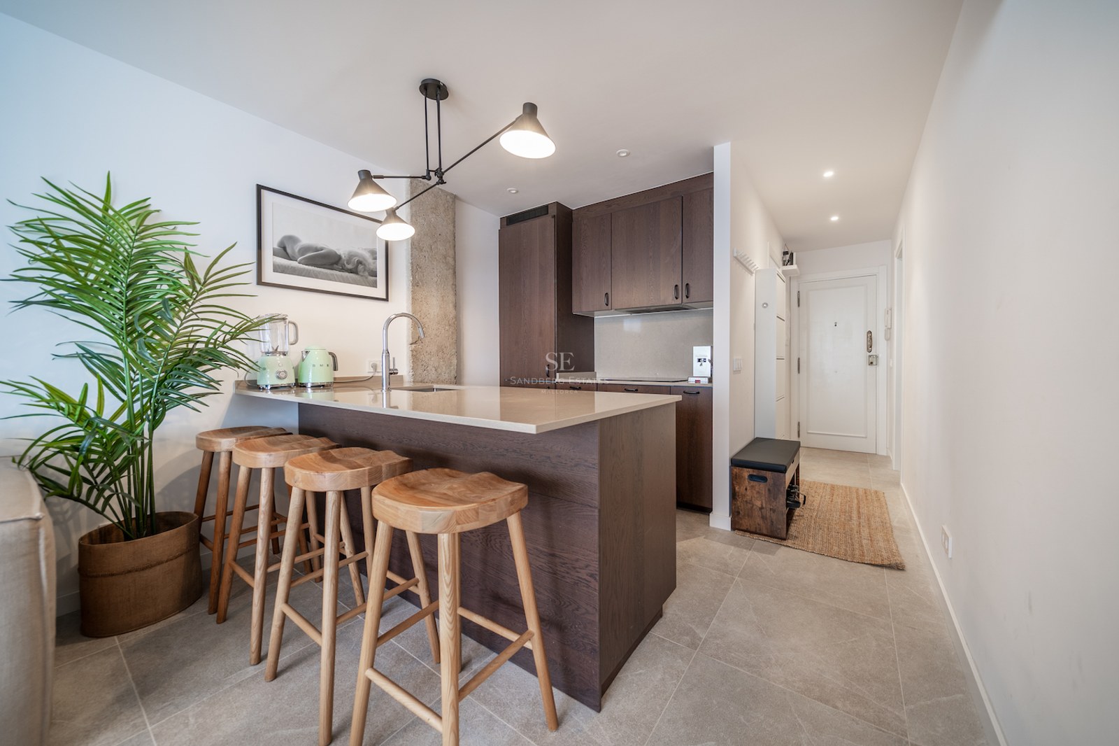 Cuisine moderne avec placards en bois sombre, îlot en pierre avec quatre tabourets et suspension industrielle.