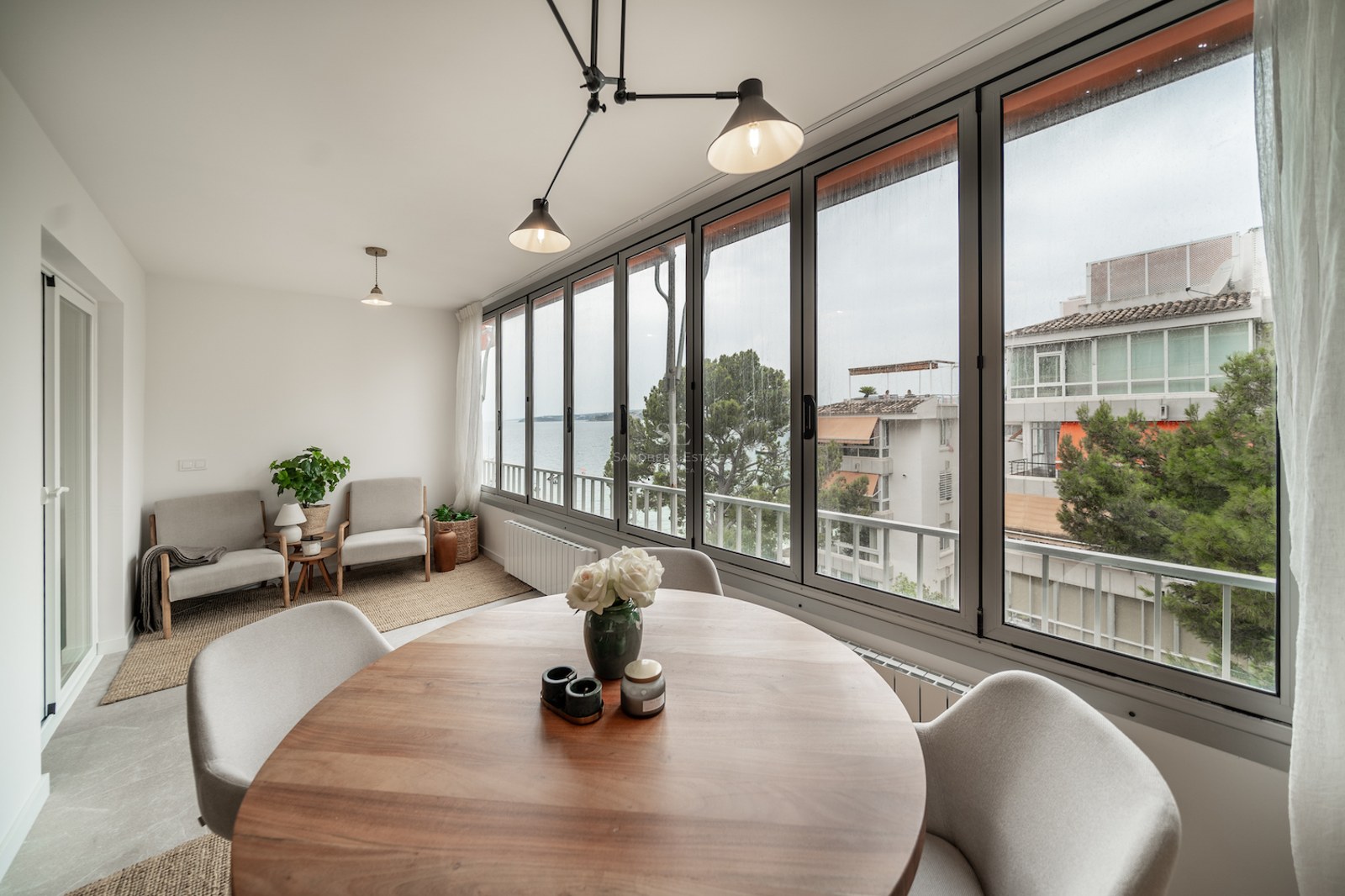 Salle à manger moderne avec table ronde en bois, grandes baies vitrées et vue sur la côte méditerranéenne.