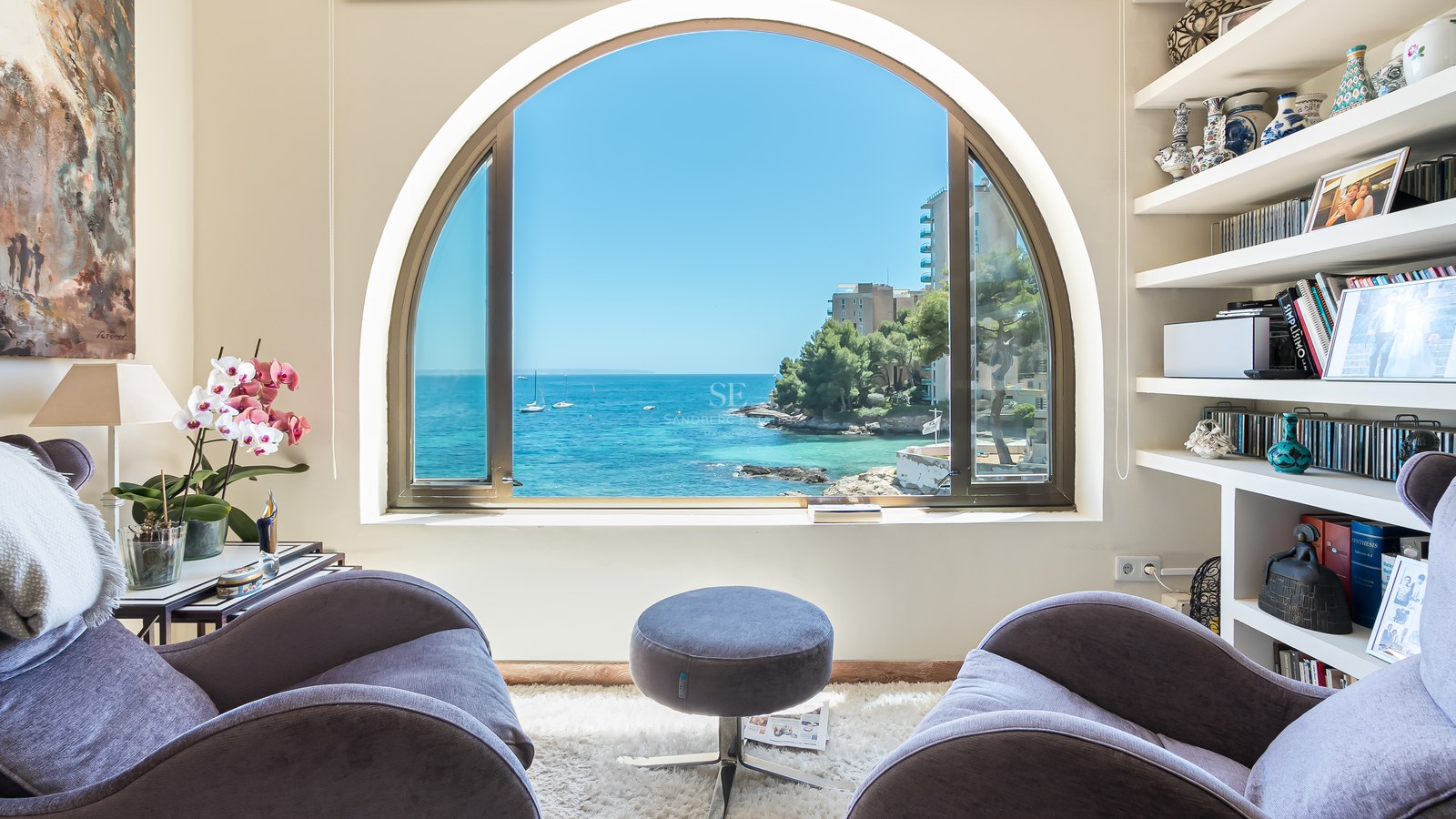 Deux fauteuils en velours face à une grande fenêtre en plein cintre donnant sur une baie méditerranéenne avec des bateaux.