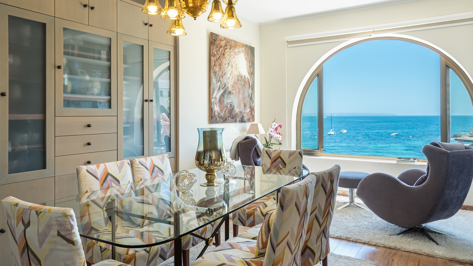 Salle à manger avec table en verre et grande fenêtre en arche offrant une vue sur la mer Méditerranée.