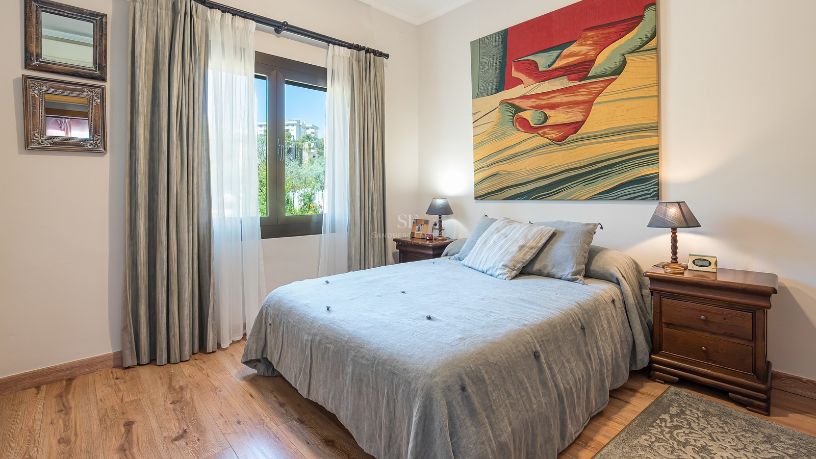 Chambre lumineuse avec parquet, lit aux draps gris, tables de chevet en bois et grand tableau coloré.