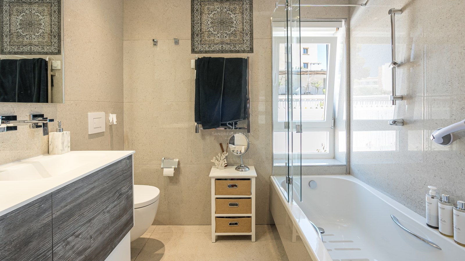 Salle de bain moderne avec baignoire blanche, paroi en verre, meuble en bois et carrelage mural effet pierre naturelle.
