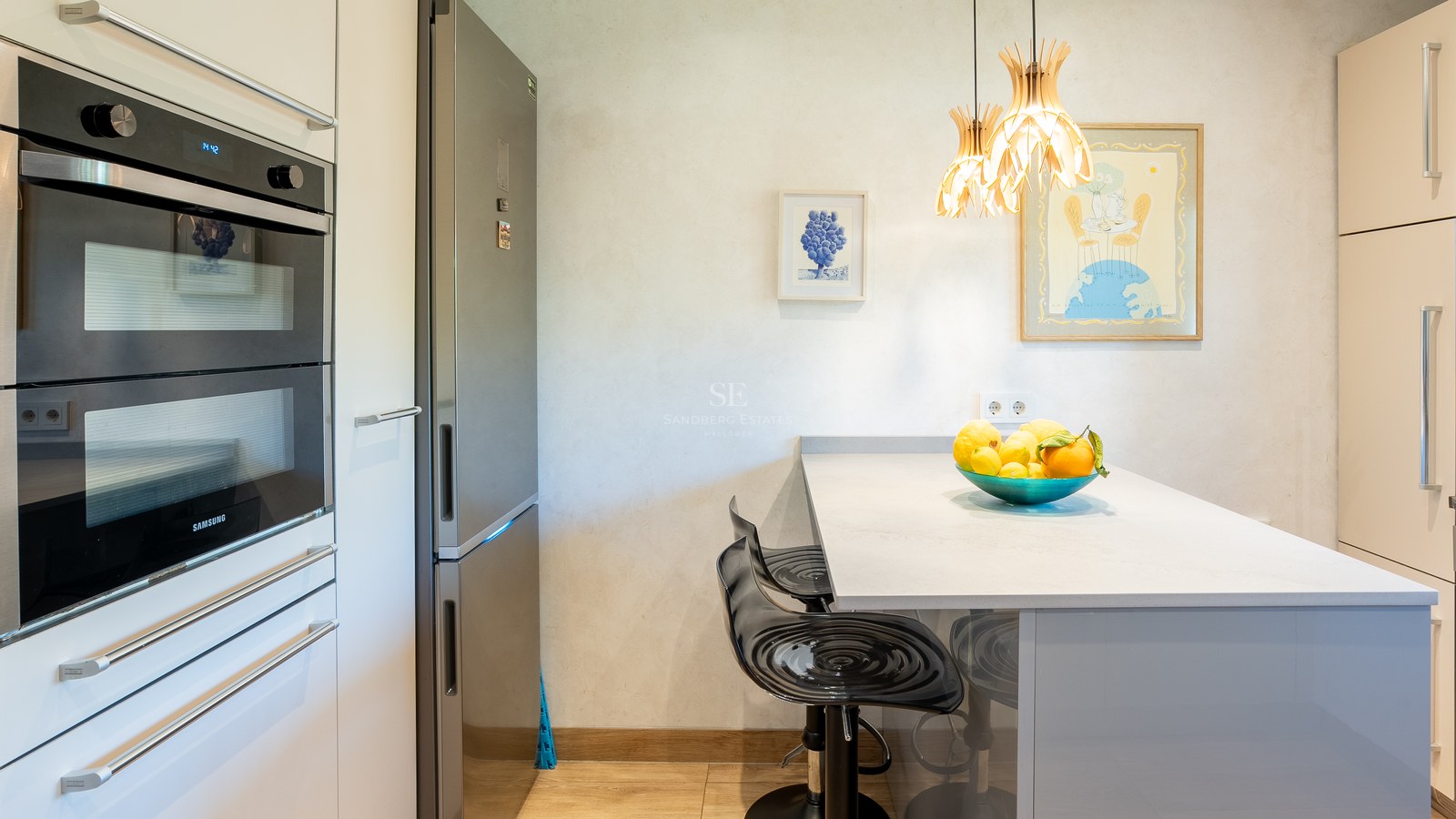 Vue d'une cuisine contemporaine avec double four Samsung, réfrigérateur inox et îlot avec tabourets de bar noirs.