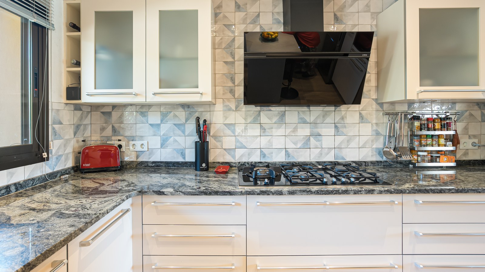 Détail d'une cuisine moderne avec plan de travail en granit, plaque de cuisson au gaz et crédence en carreaux bleus.
