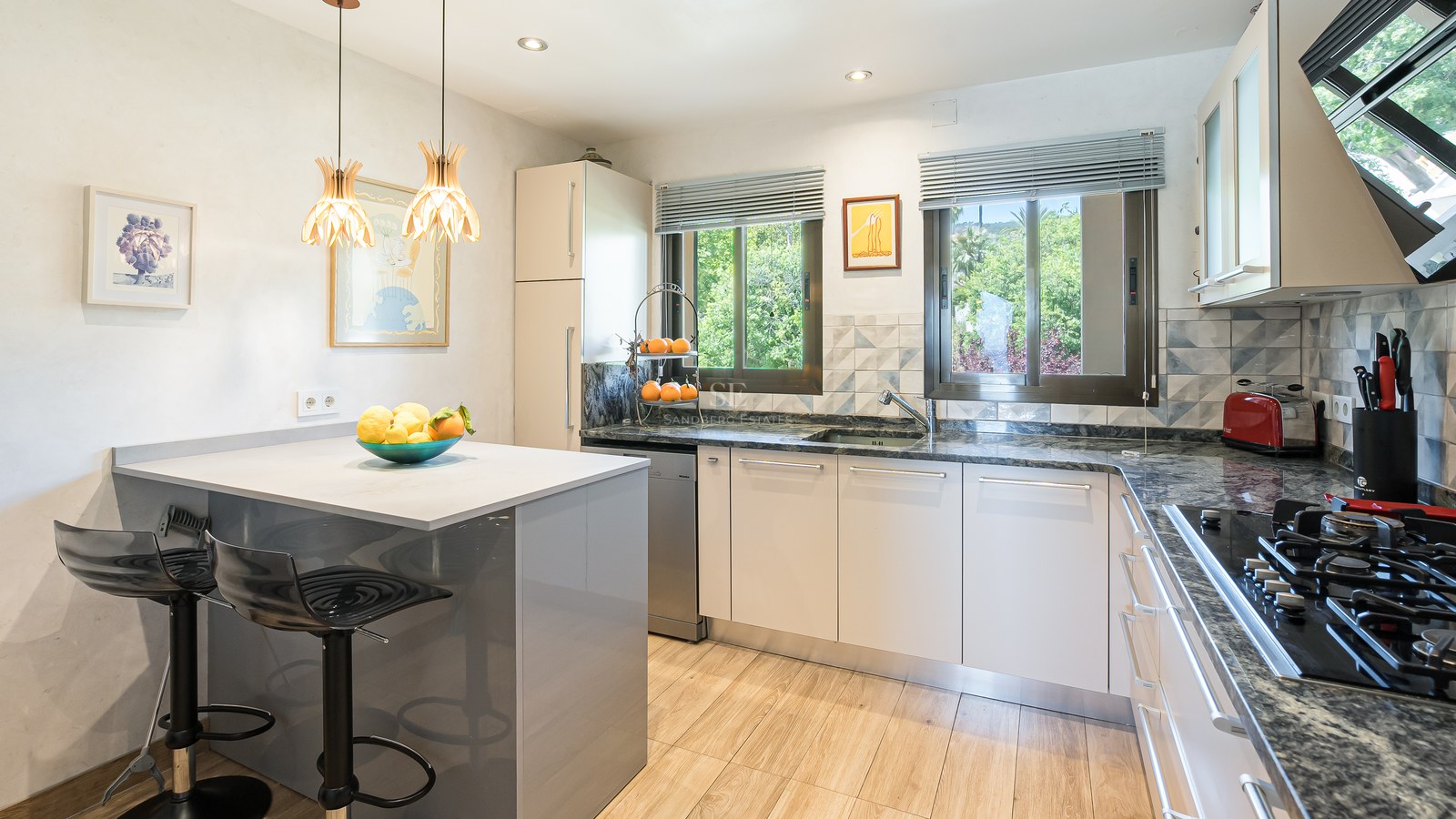 Cuisine moderne avec placards blancs, plans de travail en granit, îlot et fenêtres donnant sur la verdure.