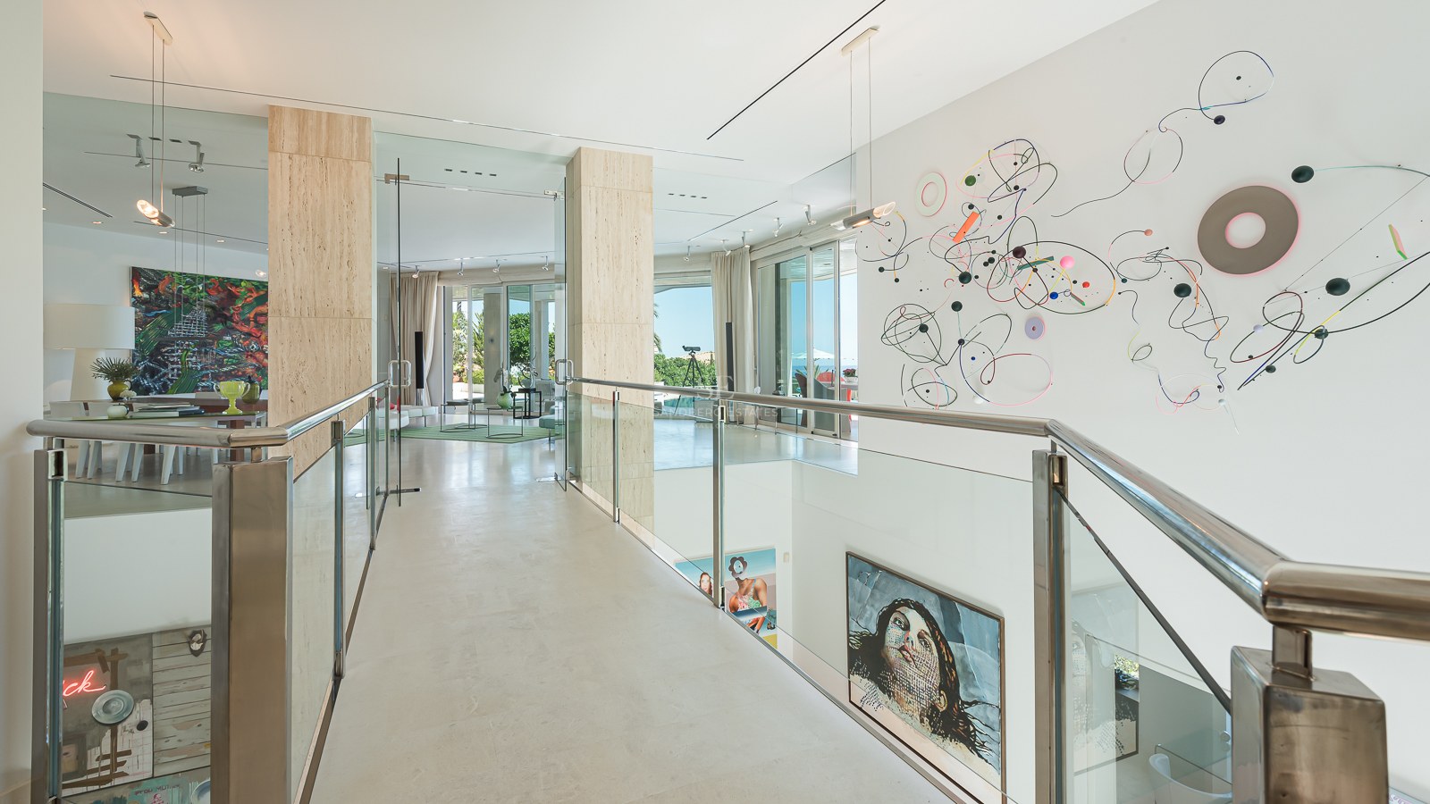 A modern upper-floor gallery featuring glass railings, travertine columns, and large-scale contemporary wall art.