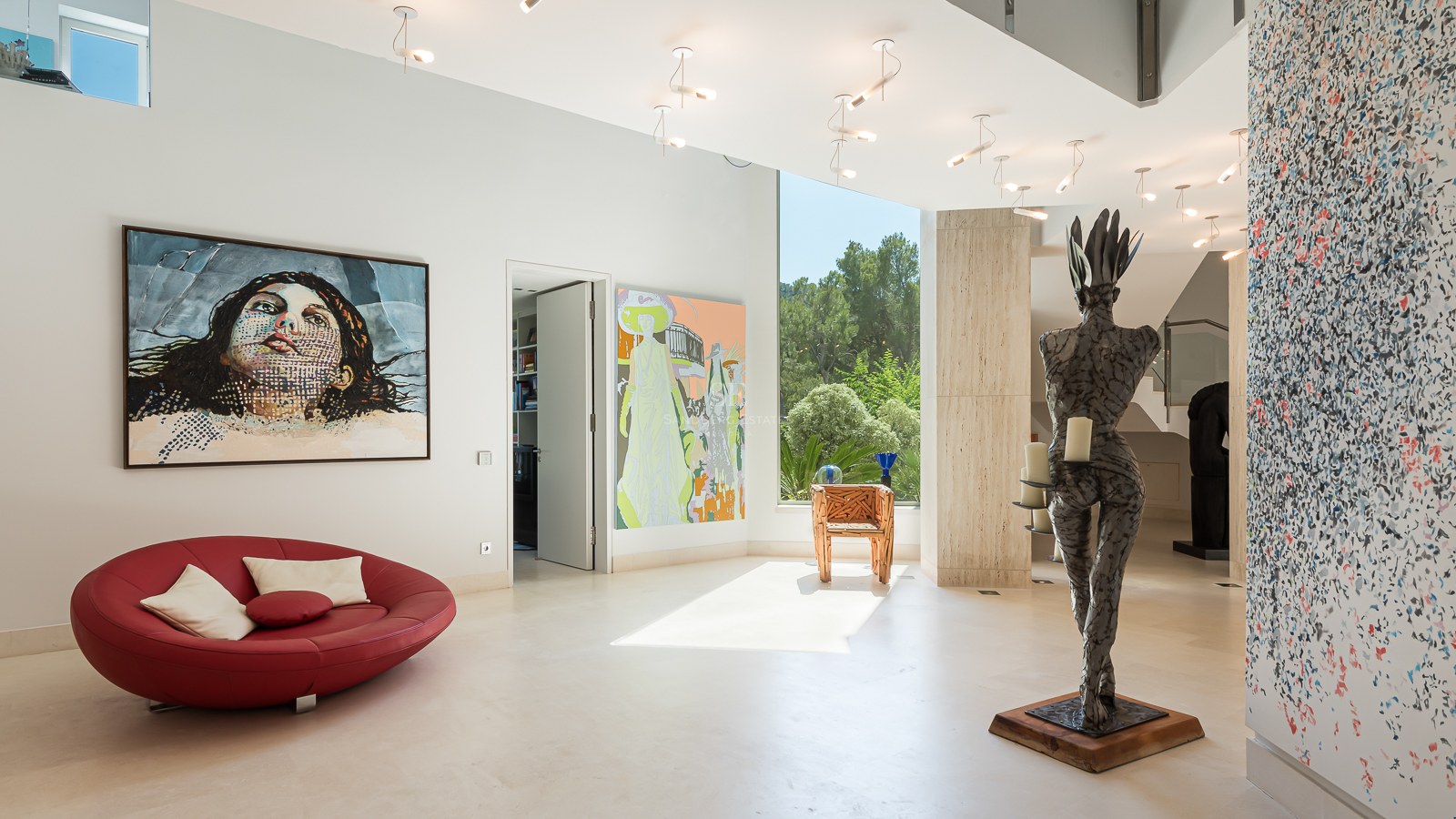 Modern white hallway with large pop-art paintings, a red circular lounge chair, and a floor-to-ceiling window.