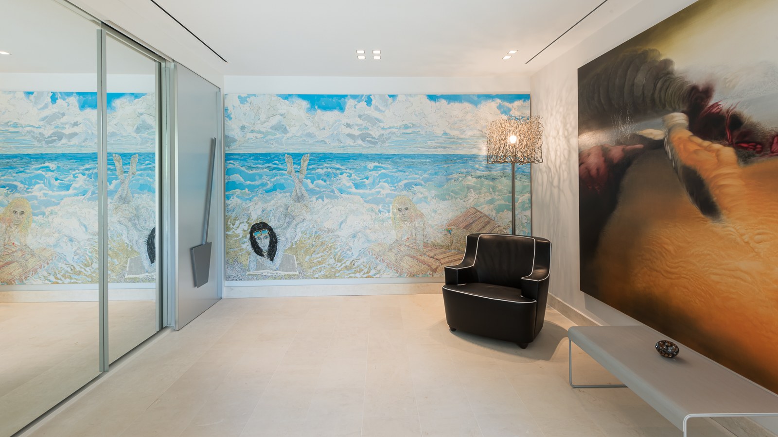Modern hallway featuring large-scale paintings, a black leather armchair, and light natural stone flooring.