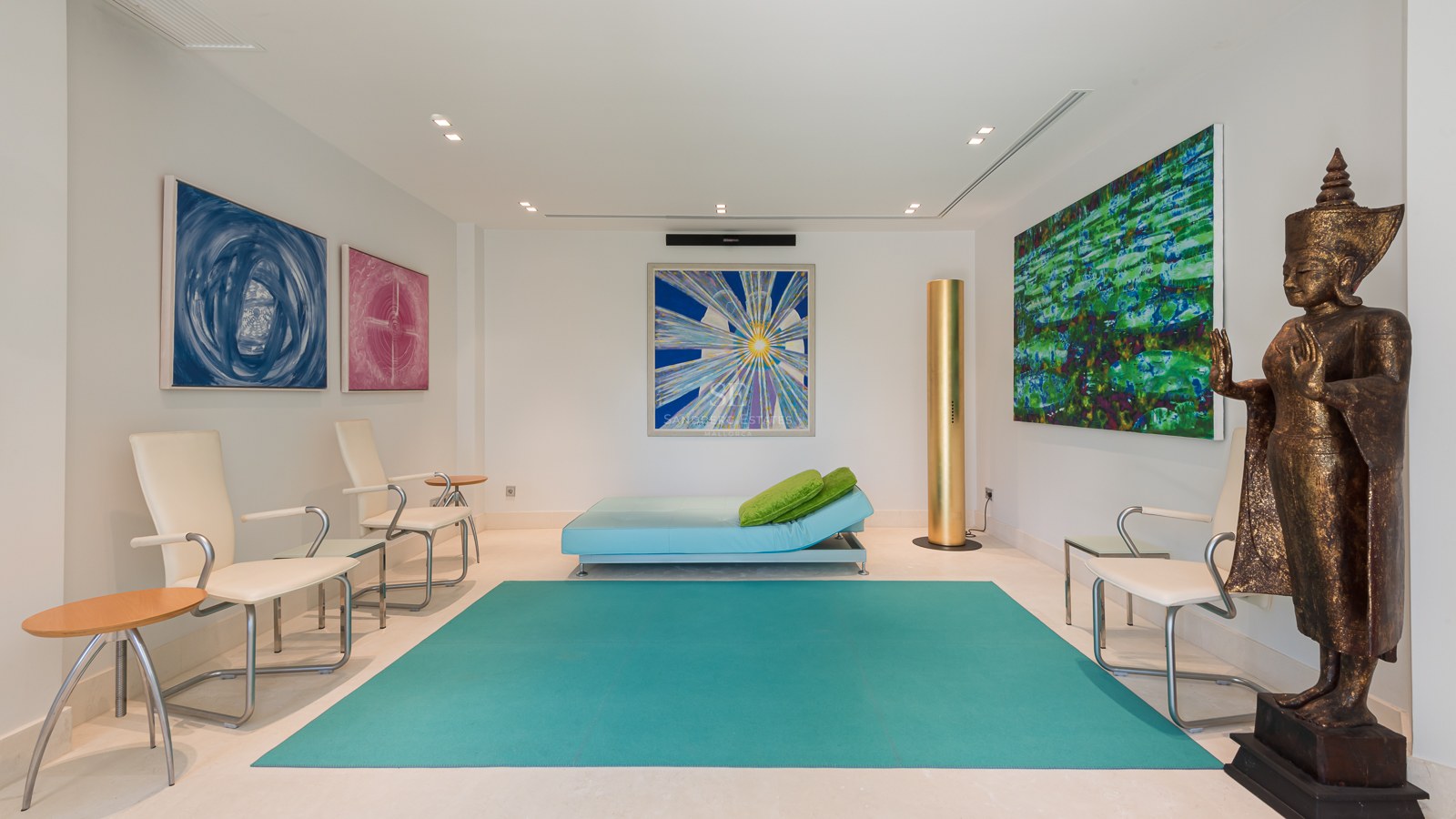 Modern relaxation room featuring a turquoise rug, an Oriental bronze statue, vibrant abstract art, and minimalist white seating.