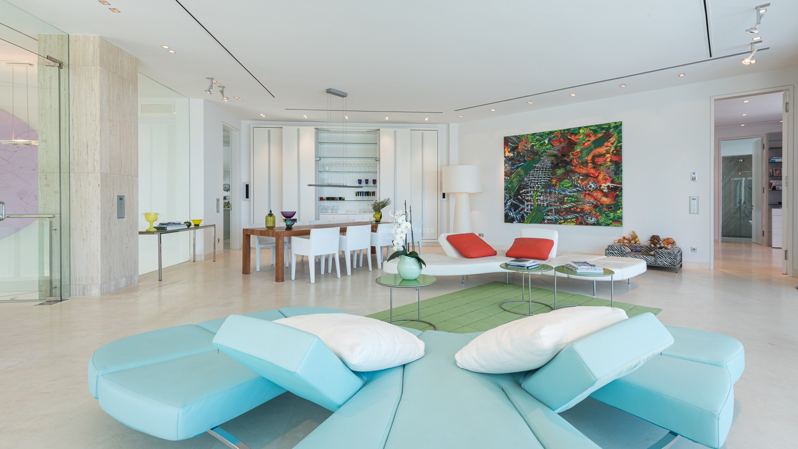 Spacious modern living room with turquoise sectional sofa, marble floors, and integrated dining area with designer furniture.