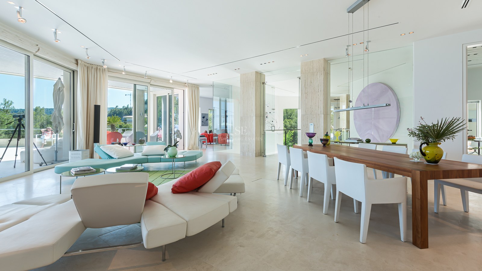 Spacious modern living room with cream stone floors, large glass windows, white leather sofas and a wood dining table.