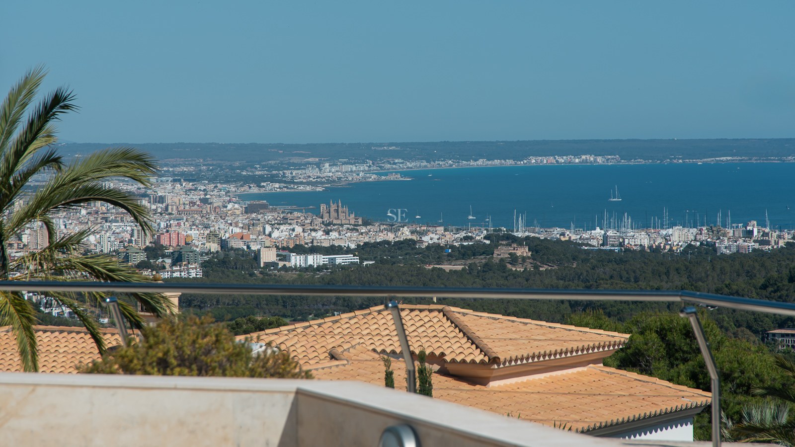 Elevated view of Palma de Mallorca bay, the cathedral, and harbor from a terrace with a glass railing.