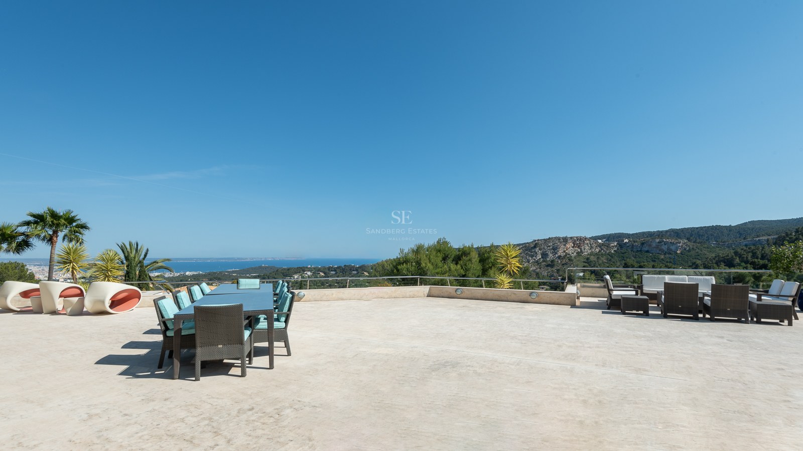 Spacious stone-paved terrace with outdoor dining and lounge areas overlooking the Mediterranean coast.
