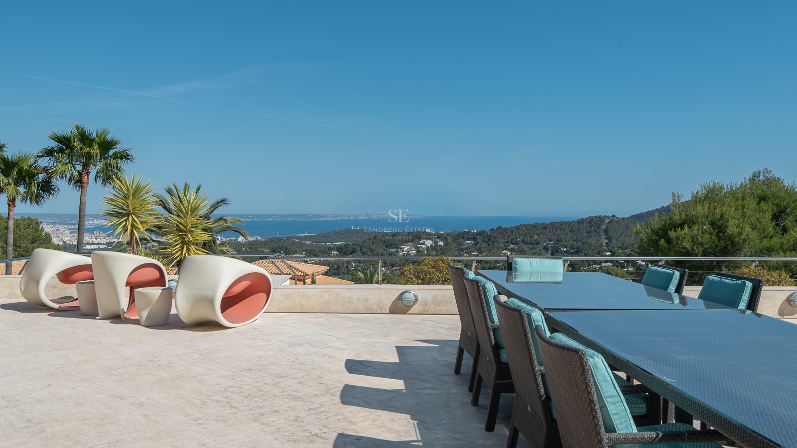 Expansive natural stone terrace with a glass dining table and modern lounge chairs overlooking the bay and mountains.