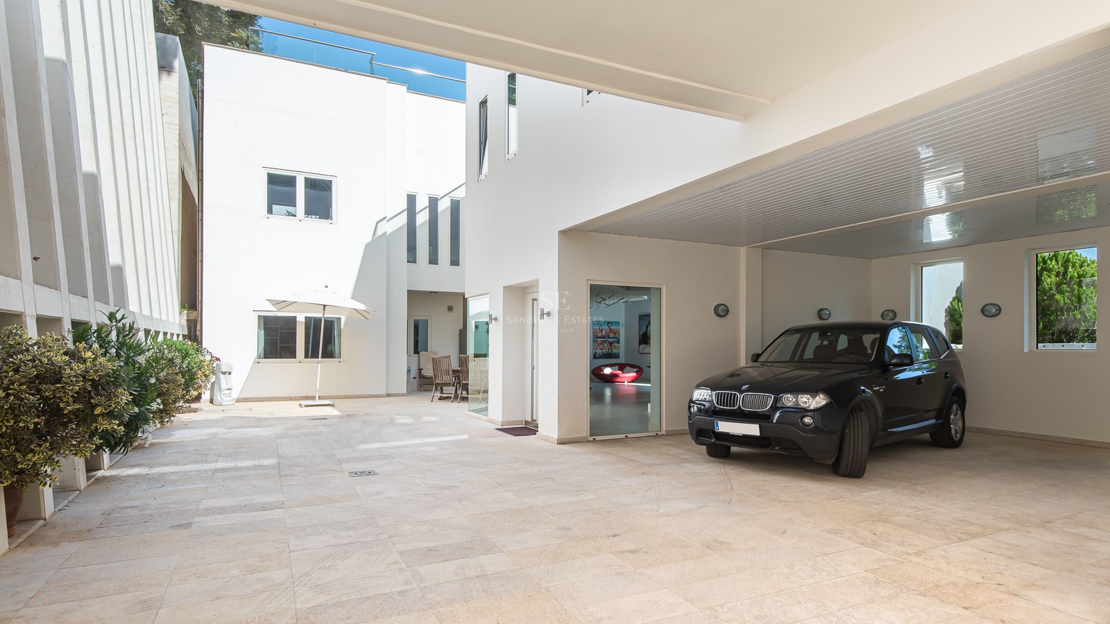 Black SUV parked in a white-walled carport with natural stone paving and bright minimalist architecture.