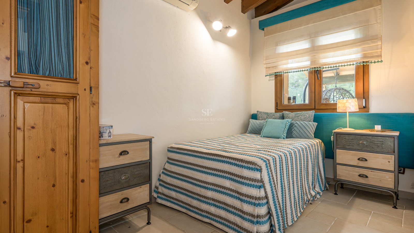 Une chambre avec un lit à rayures, une tête de lit turquoise, des meubles en bois et des tables de chevet industrielles.