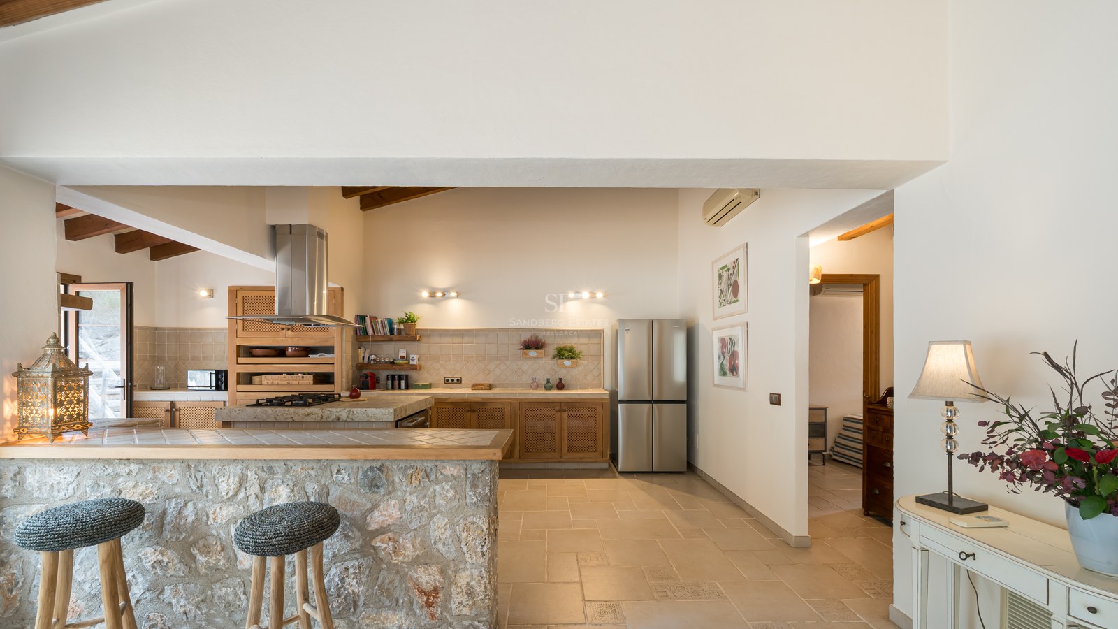 Cuisine spacieuse avec un bar en pierre naturelle, des tabourets, des poutres en bois et des appareils en inox.