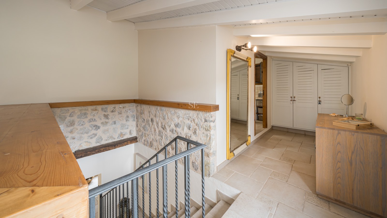Palier intérieur avec escalier en fer, murs en pierre apparente, poutres en bois et placards intégrés blancs.