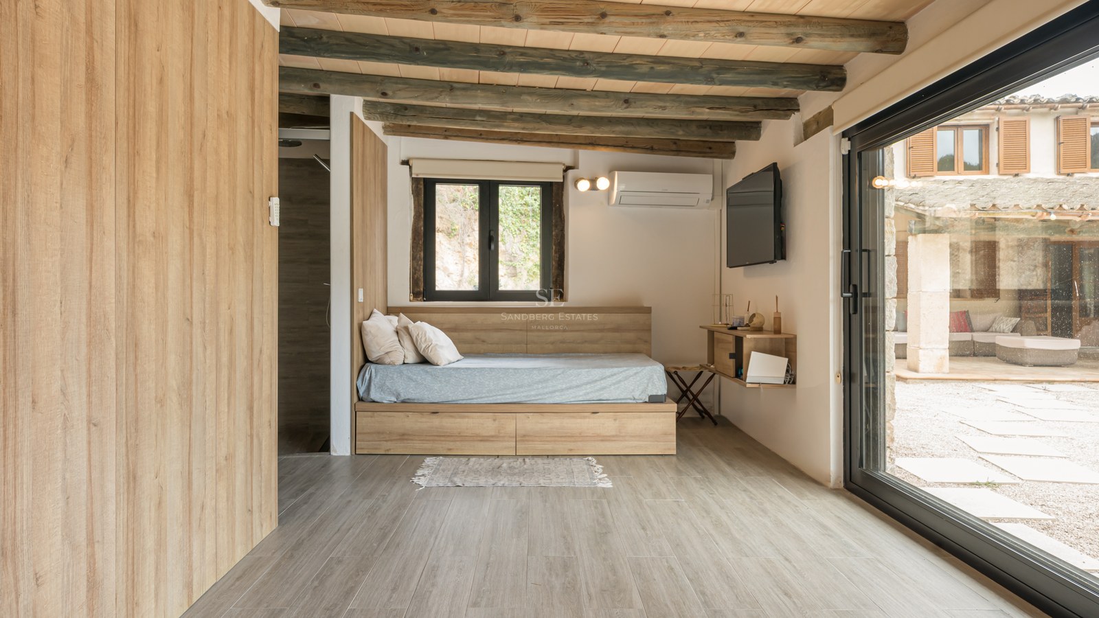 Chambre moderne avec lit plateforme en bois, poutres apparentes et grande porte vitrée donnant sur un patio.