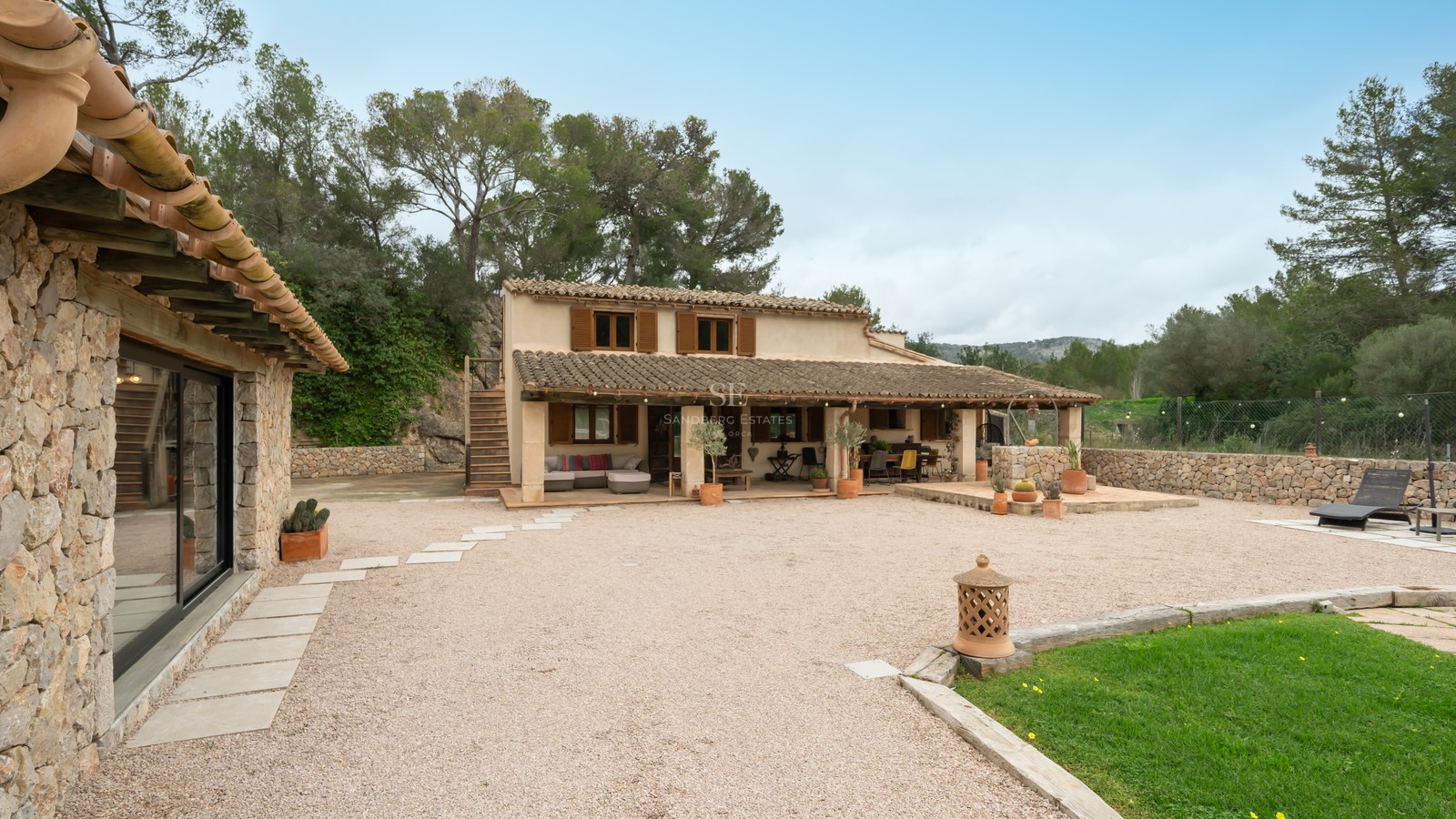 Extérieur d'une maison traditionnelle en pierre avec tuiles en terre cuite, volets en bois et cour en gravier.