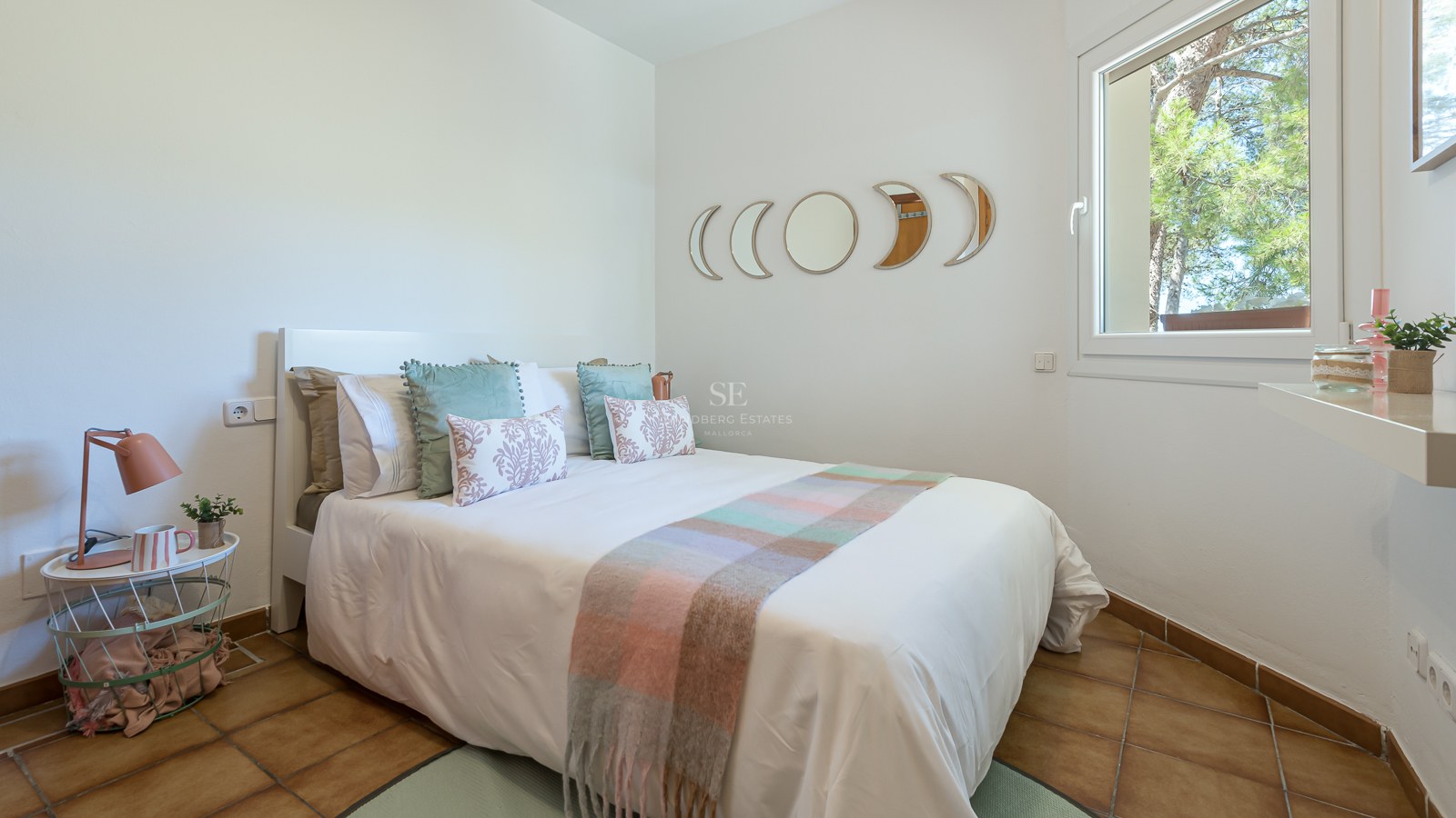 Chambre avec lit blanc, sol en terre cuite et miroirs phases de lune au-dessus de la tête de lit.