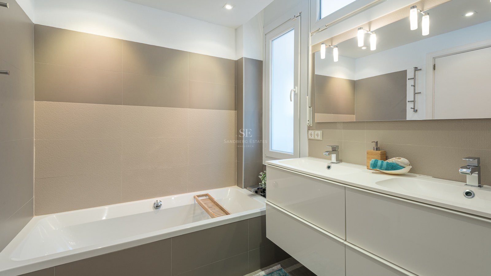 Une salle de bain contemporaine avec baignoire blanche, meuble double vasque, grands carreaux beiges et un large miroir.