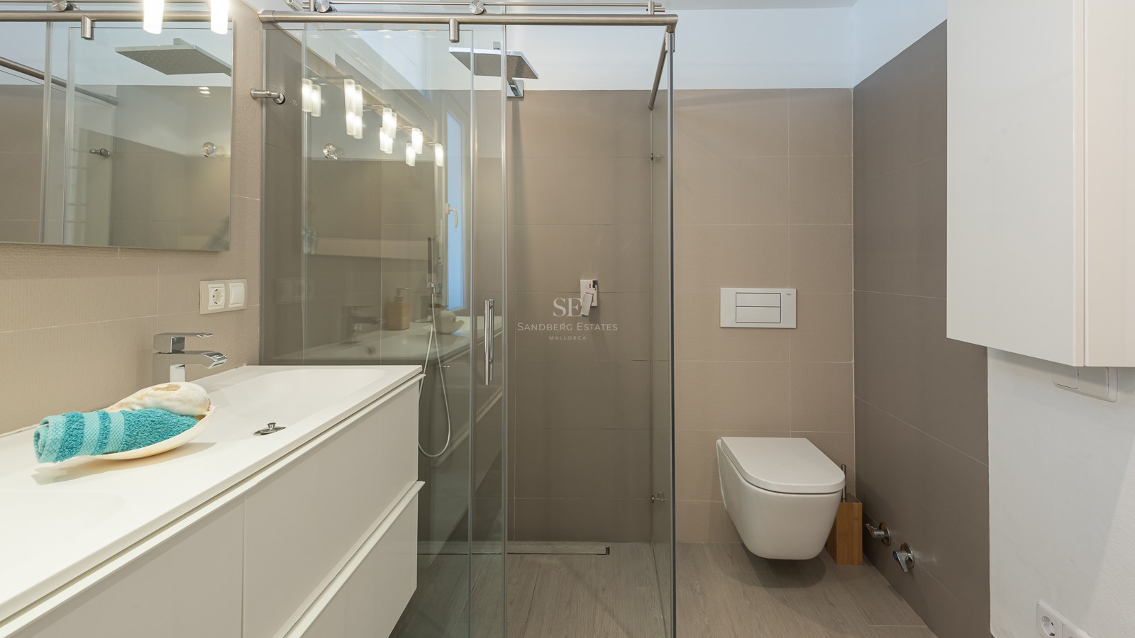 Salle de bain moderne avec meuble blanc, paroi de douche en verre et toilettes suspendues avec carrelage neutre.