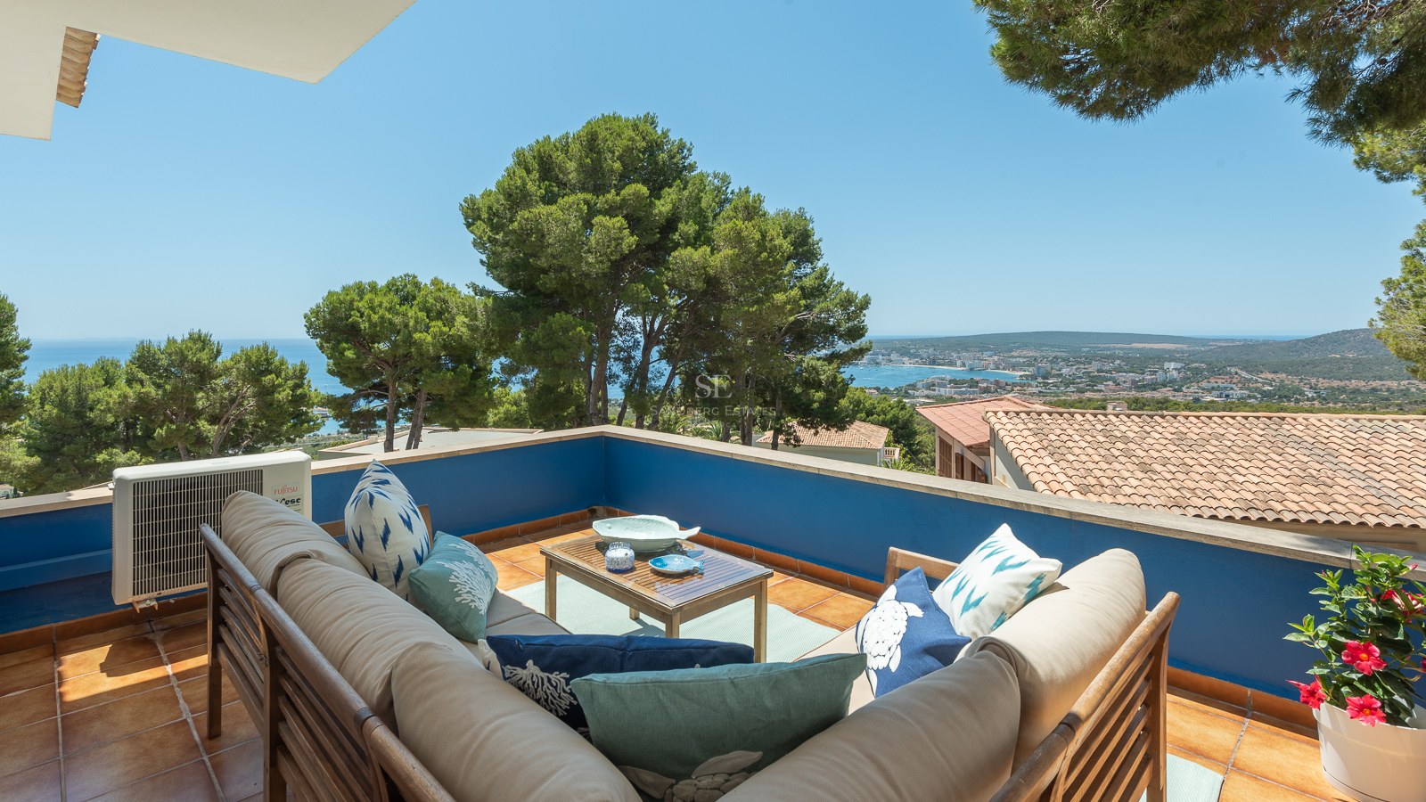 Terrasse extérieure avec canapé en L, murs bleus et vue panoramique sur la côte méditerranéenne.