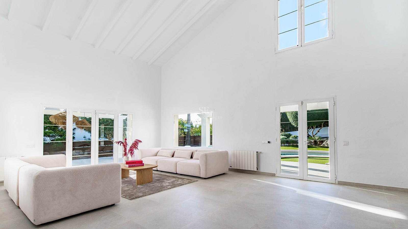 Salon spacieux aux plafonds blancs, canapés beige et portes-fenêtres ouvrant sur le jardin ensoleillé.