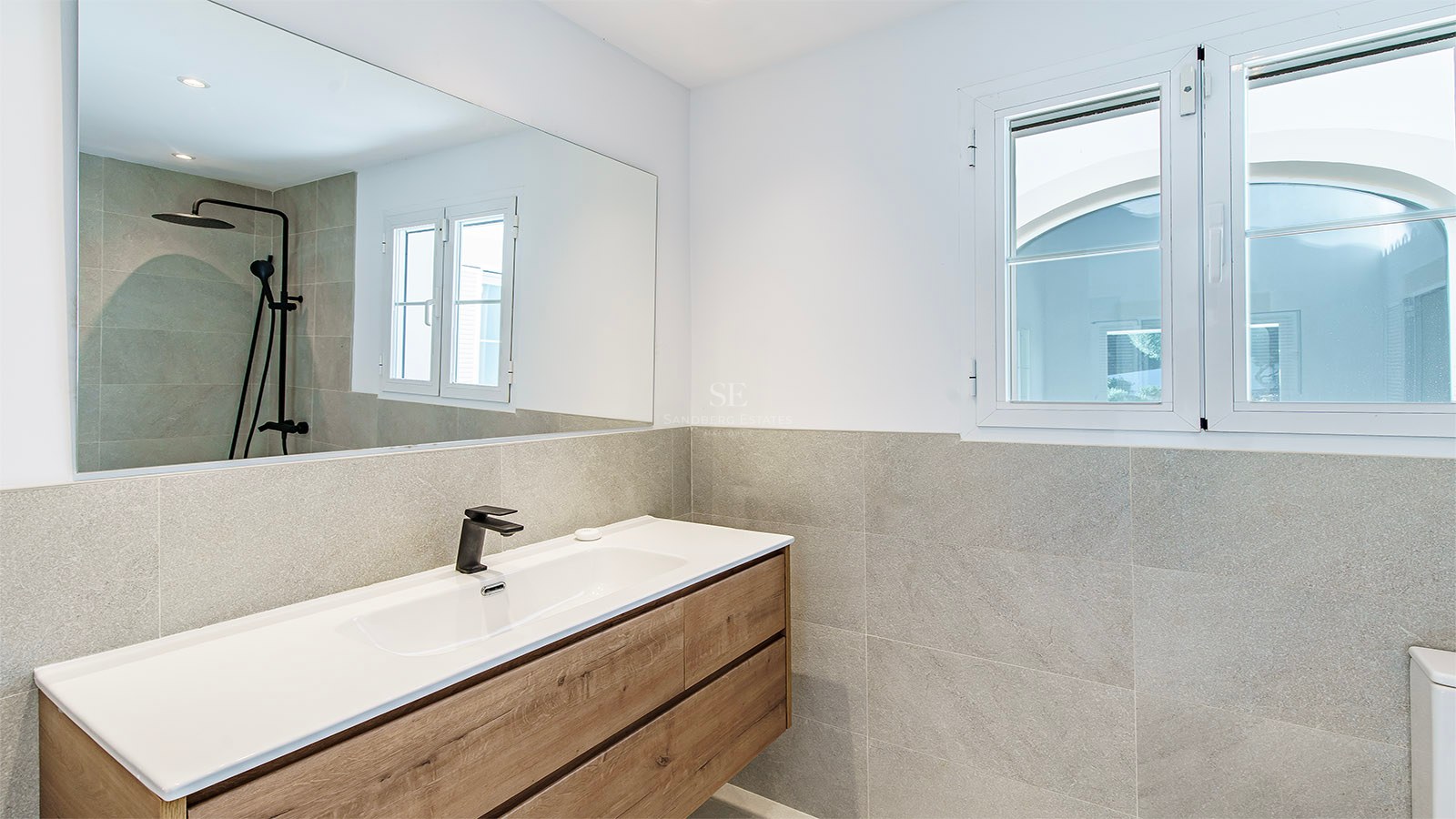 Intérieur d'une salle de bain moderne avec meuble en bois, lavabo blanc, robinetterie noire et carrelage gris.