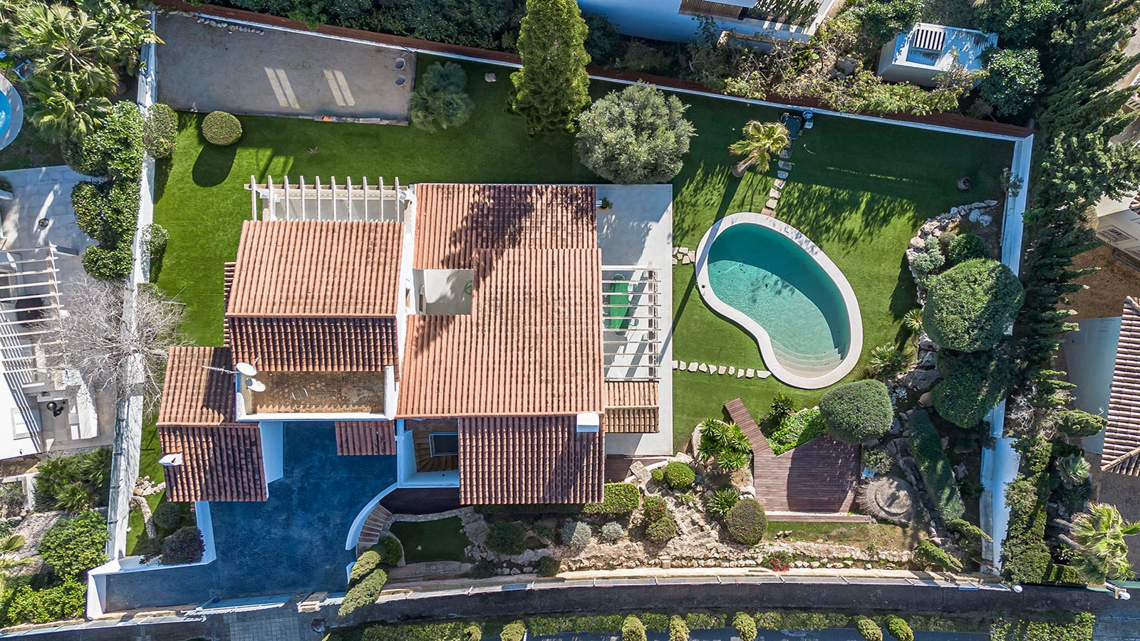 Vue plongeante d'une villa de luxe avec toit en terre cuite, piscine en forme de rein et jardins paysagers.