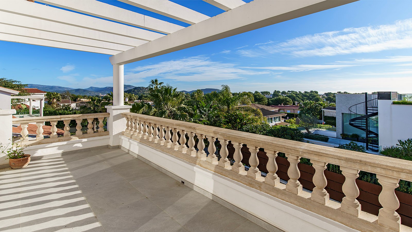 Grande terrasse avec pergola blanche, balustrade en pierre sculptée et vue sur la végétation tropicale et les montagnes.