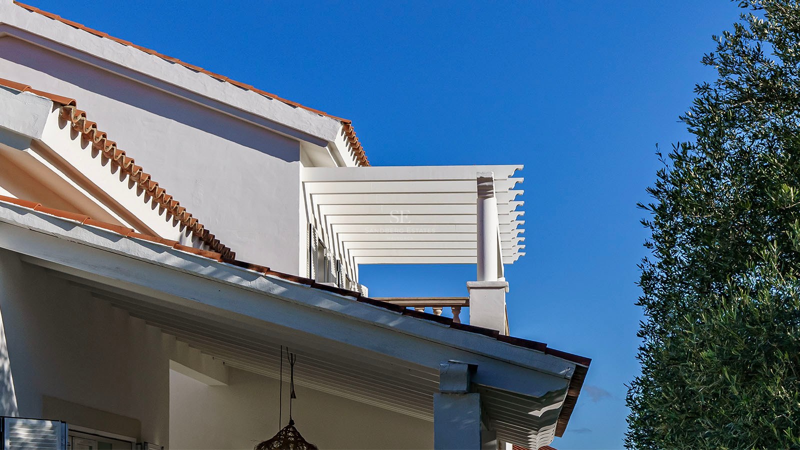 Détail de façade d'une villa blanche avec pergola, tuiles en terre cuite et ciel bleu azur.