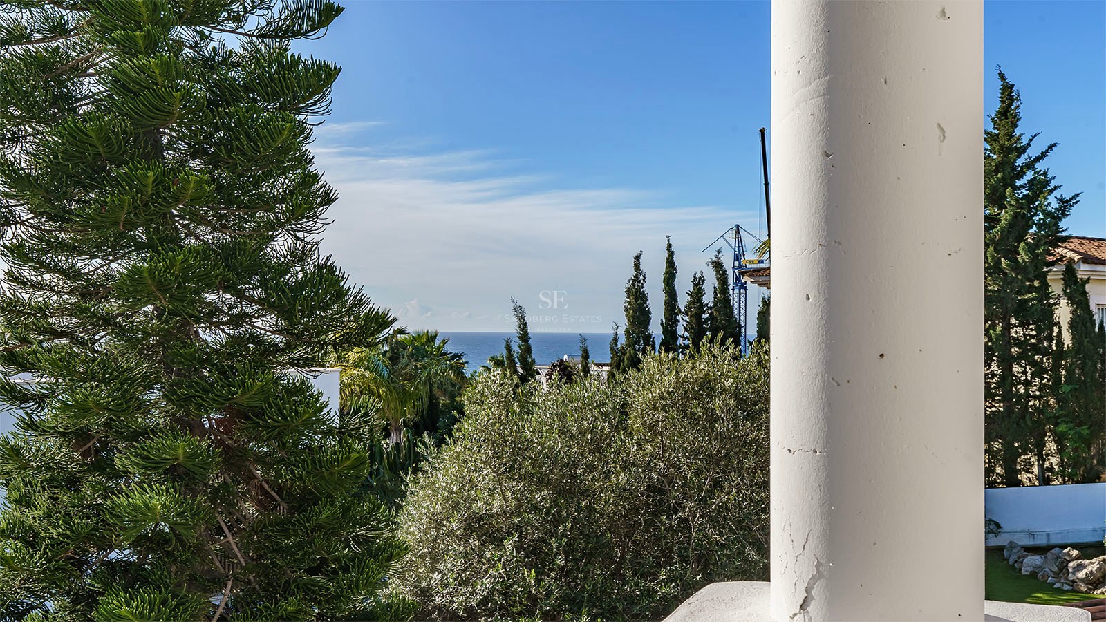 Vue sur la mer Méditerranée encadrée par une colonne blanche et une végétation luxuriante sous un ciel bleu.