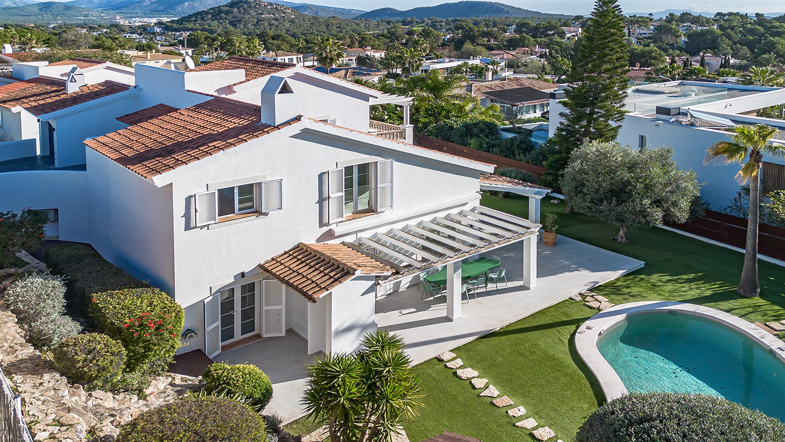 Vue aérienne d'une villa blanche avec toit en tuiles, jardin verdoyant, pergola et piscine privée.