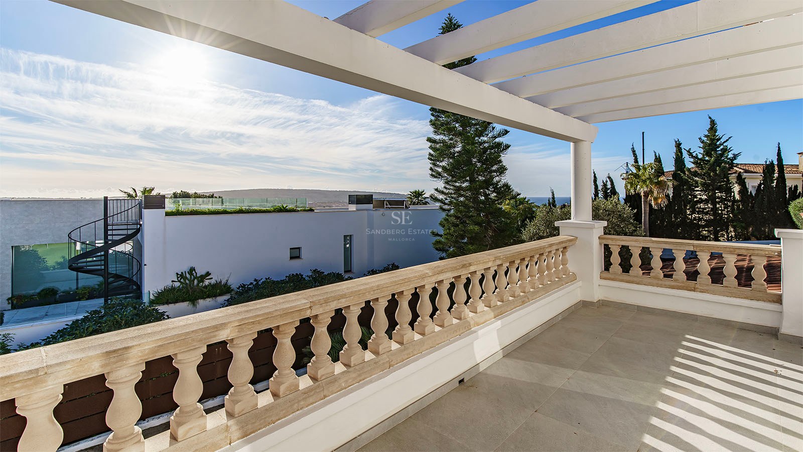 Grande terrasse avec balustrade en pierre et pergola blanche offrant une vue sur le paysage côtier.